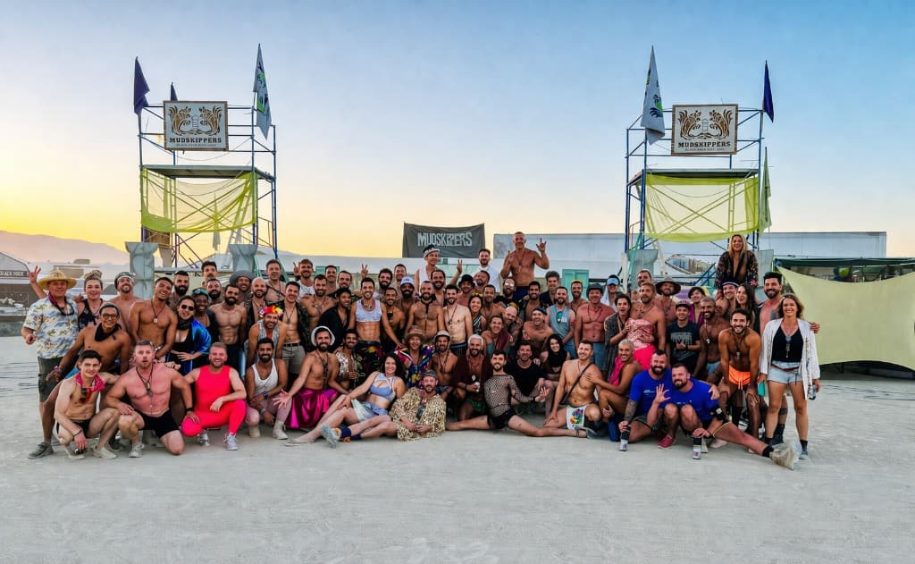 Mudskippers Camp gathered on the playa at sunset, in front of two scaffolding towers