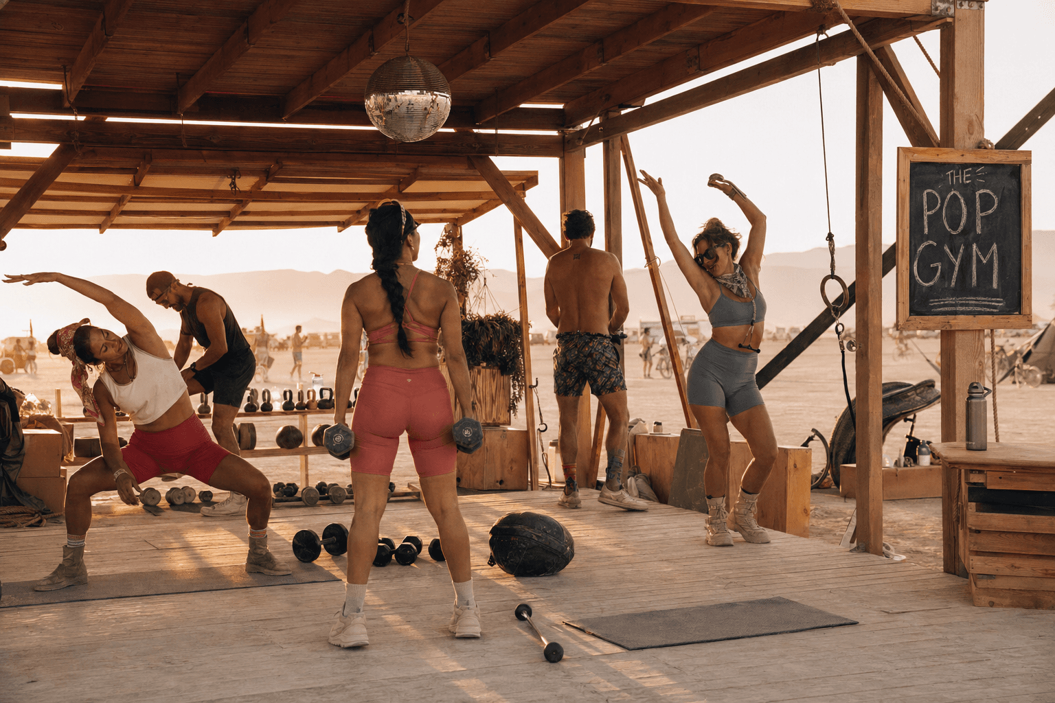The Pop Gym at sunrise on the playa, with kettlebells, mats, and a disco ball